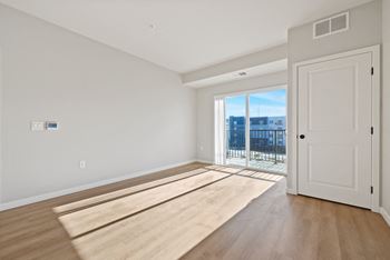A room with a white door and a window with a view of a balcony.