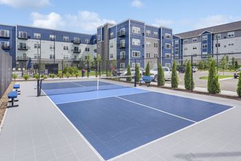 A tennis court is surrounded by apartment buildings.