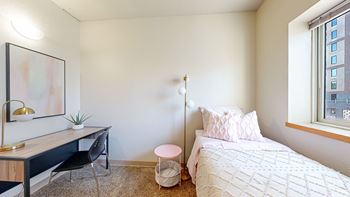 A bedroom with a bed and a desk and a window