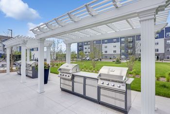 A white pergola is over a grill and table.