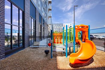 A playground with a bright orange slide in front of a building