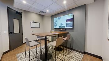 A conference room with a table, chairs, and a screen displaying a presentation.