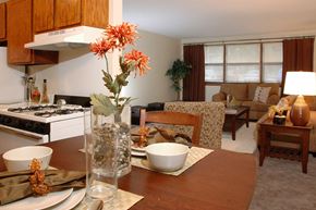 Brooklyn Park apartment for rent - a living room with a wooden table and a kitchen in the background at Point of America Apartments,Brooklyn Park, Minnesota