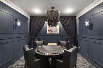 A black poker table is surrounded by black chairs in a room with dark walls.