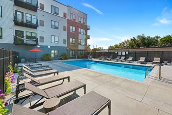 A swimming pool with lounge chairs and umbrellas in front of an apartment building