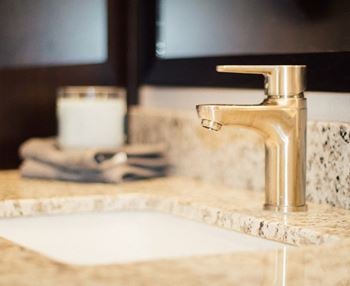A bathroom sink with a gold faucet and a white candle on the counter.