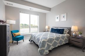 Maple Grove apartment for rent - A bedroom with a large bed and a blue chair.at The Edison at Maple Grove, Maple Grove, MN