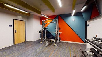 A gym room with a treadmill, weights and a wall with a blue and orange design.