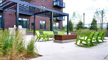 A patio with green chairs and a bench in front of a building.