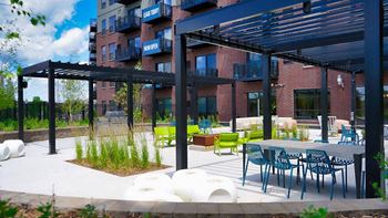 A patio area with tables and chairs is covered by a black awning.