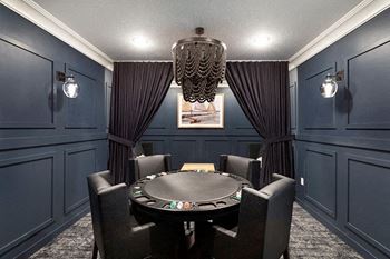 A black poker table is surrounded by chairs in a room with dark walls.