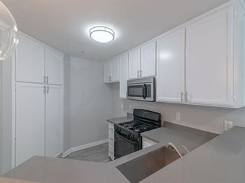 An empty kitchen with white cabinets and a stove and microwave