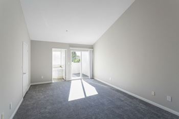 A carpeted living room with white walls and a door to a bathroom