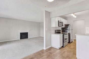 An empty living room with a kitchen and a fireplace