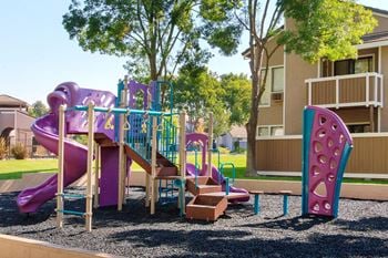 A playground with a slide and other toys in front of an apartment building