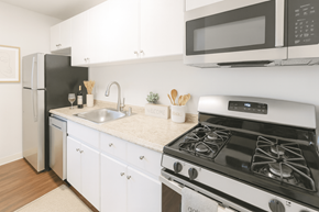 Concord apartment for rent - A modern kitchen with a black fridge, white cabinets, and a white stove top oven.