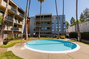 Concord apartment for rent - A swimming pool in front of a multi-story apartment building with palm trees.