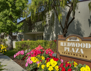 Fremont apartment for rent - A sign for Redwood Plaza Apartments is in front of a building with a flower bed in the foreground.