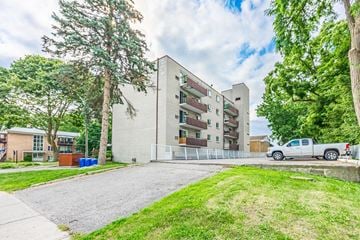 Whitby apartment for rent - A large building with a white exterior is surrounded by trees and a white pickup truck is parked in front.