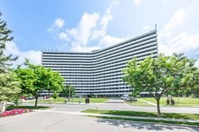North York apartment for rent - A large, modern building with a curved facade is surrounded by a well-maintained lawn and trees.