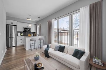 Kitchener apartment for rent - A modern living room with a white sofa and a kitchen area in the background.
