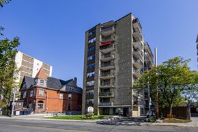 Toronto apartment for rent - A tall apartment building with balconies is in the foreground of a street scene.