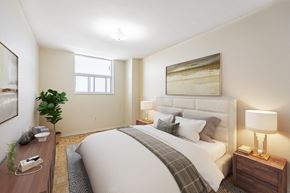 Mississauga apartment for rent - A well-lit bedroom with a large bed, a nightstand with a lamp, and a potted plant.