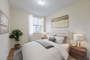 North York apartment for rent - A well-lit bedroom with a large bed, a nightstand with a lamp, and a potted plant.