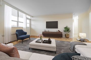 North York apartment for rent - A living room with a blue chair, a grey sofa, a white couch, and a television on the wall.