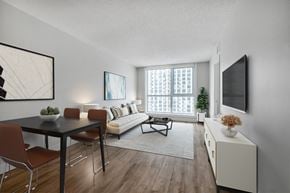 Toronto apartment for rent - A living room with a black table and chairs, a white sofa, and a television on the wall.