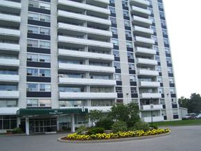 North York apartment for rent - A large white building with a green awning and a flower bed in front.