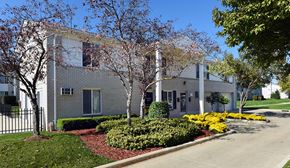 Sterling Heights apartment for rent - A white building with a black fence and trees in front.