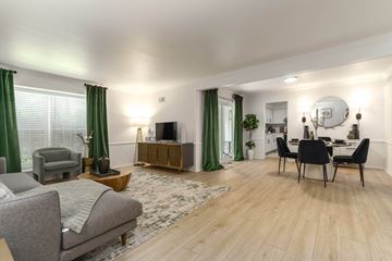 Farmington Hills townhouse for rent - A living room with a grey sofa, a wooden coffee table, a TV, a dining table with chairs, and a rug.