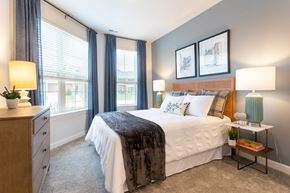 Commerce Township apartment for rent - A bedroom with a large bed and a nightstand with a lamp.