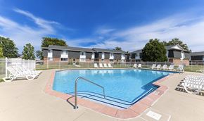 Madison Heights apartment for rent - A swimming pool surrounded by chairs and a fence with houses in the background.