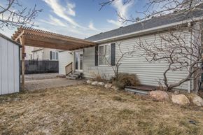 West Jordan apartment for rent - A house with a grey siding and a white door is surrounded by a fence and a small tree.