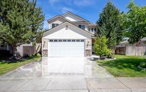 Nampa apartment for rent - A two-story house with a garage is surrounded by a fence and trees.