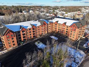 Moncton apartment for rent - A large red building with a grey roof and a parking lot in front.