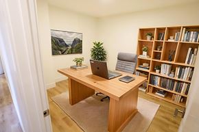 Moncton apartment for rent - A room with a desk, a laptop, a phone, a potted plant, and a bookshelf.