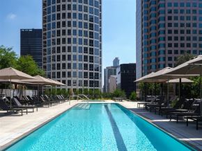 Los Angeles apartment for rent - A swimming pool surrounded by lounge chairs and umbrellas with a city skyline in the background.