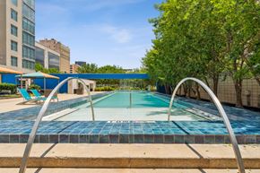 Dallas apartment for rent - A blue tiled pool surrounded by trees and buildings.