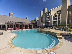 Irving apartment for rent - A large outdoor swimming pool with a stone border and a building in the background.