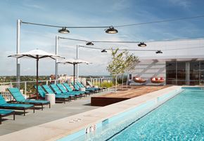 Arlington apartment for rent - A pool with blue chairs and umbrellas is surrounded by a white building.