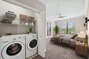 Houston apartment for rent - A laundry room with a washer and dryer and a bedroom with a bed and a ceiling fan.