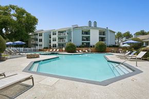 Charlotte apartment for rent - A swimming pool surrounded by lounge chairs and umbrellas in front of a multi-story apartment building.
