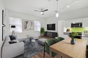 Dallas apartment for rent - A modern living room with a grey sofa, a wooden dining table, and a green chair.