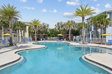 Kissimmee apartment for rent - A large swimming pool surrounded by palm trees and lounge chairs.