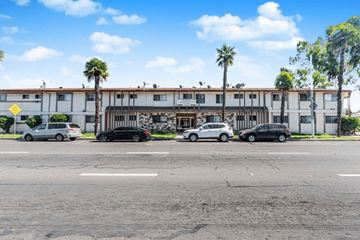 Lynwood apartment for rent - A parking lot with cars and a building with palm trees in front.