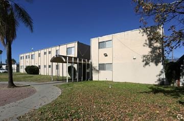 Highland apartment for rent - A building with a white and beige exterior is surrounded by a grassy area with fallen leaves.