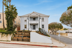 San Pedro apartment for rent - A white two-story house with a grey roof and a front yard with a wooden fence and a palm tree.